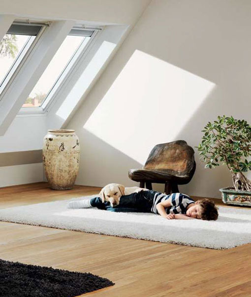 Chambre sous les toits avec deux fenêtres de toit. Un enfant dort sur un tapis blanc.