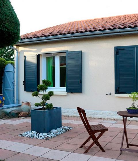 Terrasse d'une maison avec des volets battants bleus foncés. La maison est basse et fait penser aux maisons provençales.